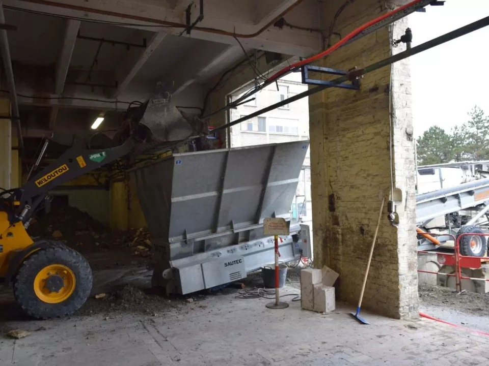 A loader discharging spoil into the hopper of a rubble conveyor.